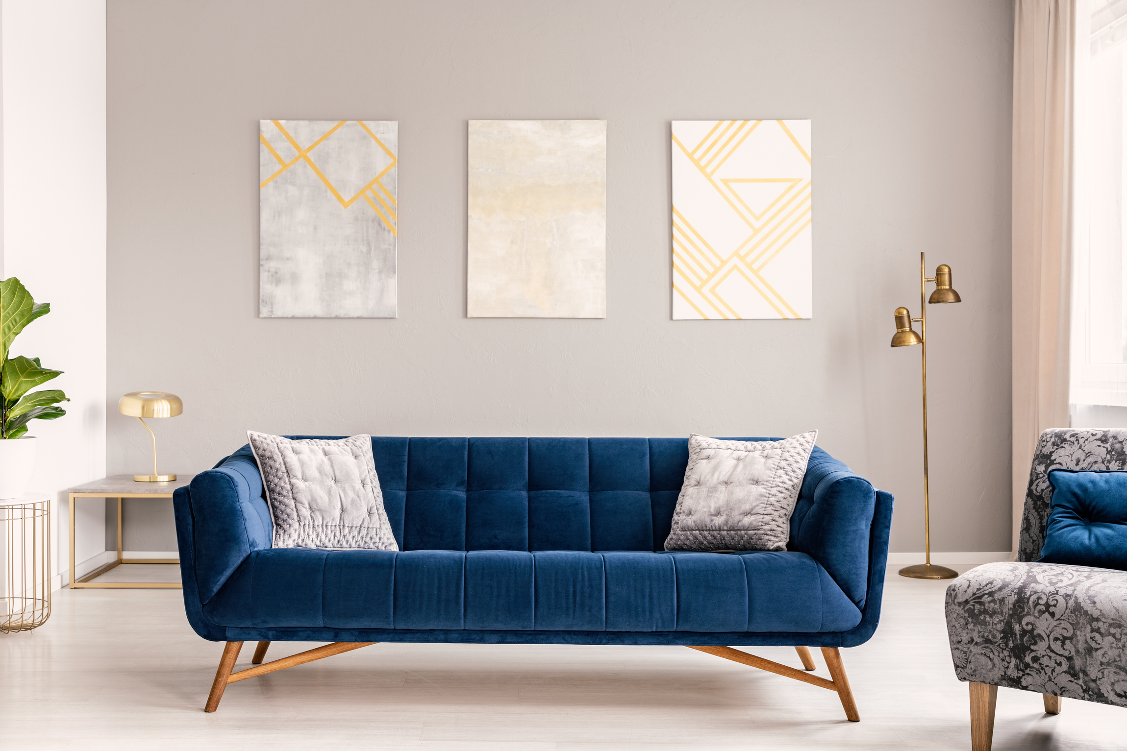Elegant living room interior with a comfortable big blue velvet sofa and gold decorations. Real photo.